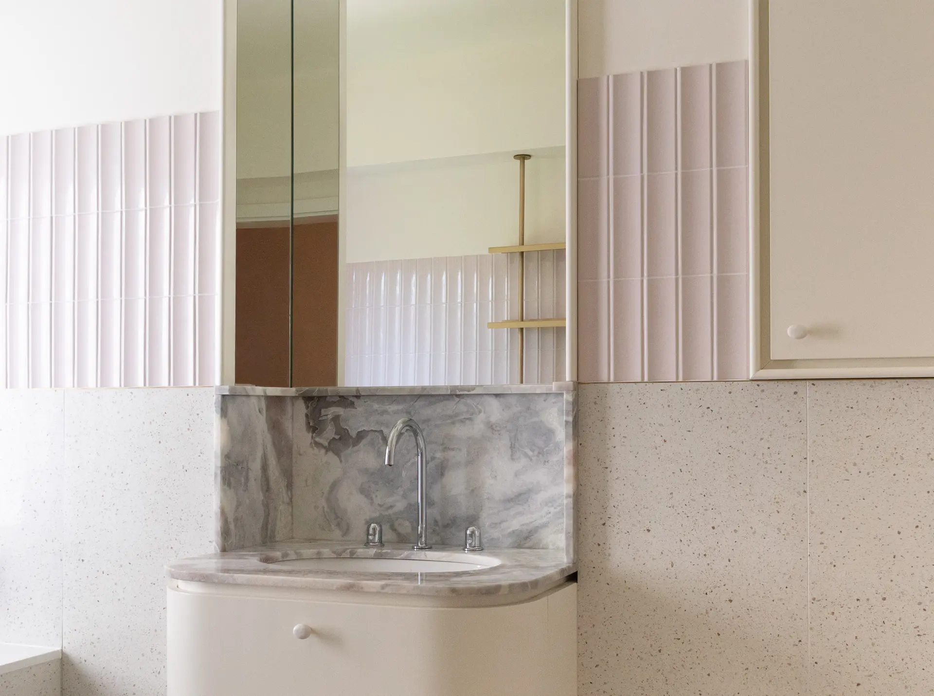 Baie cu plăci ceramice roz-pastel, lavoar rotunjit și oglindă